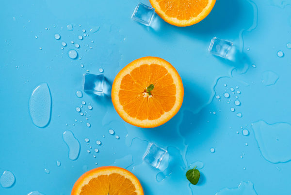 Am image of an orange cut in hald on a blue surface showing ice cubes and puddles of water on it